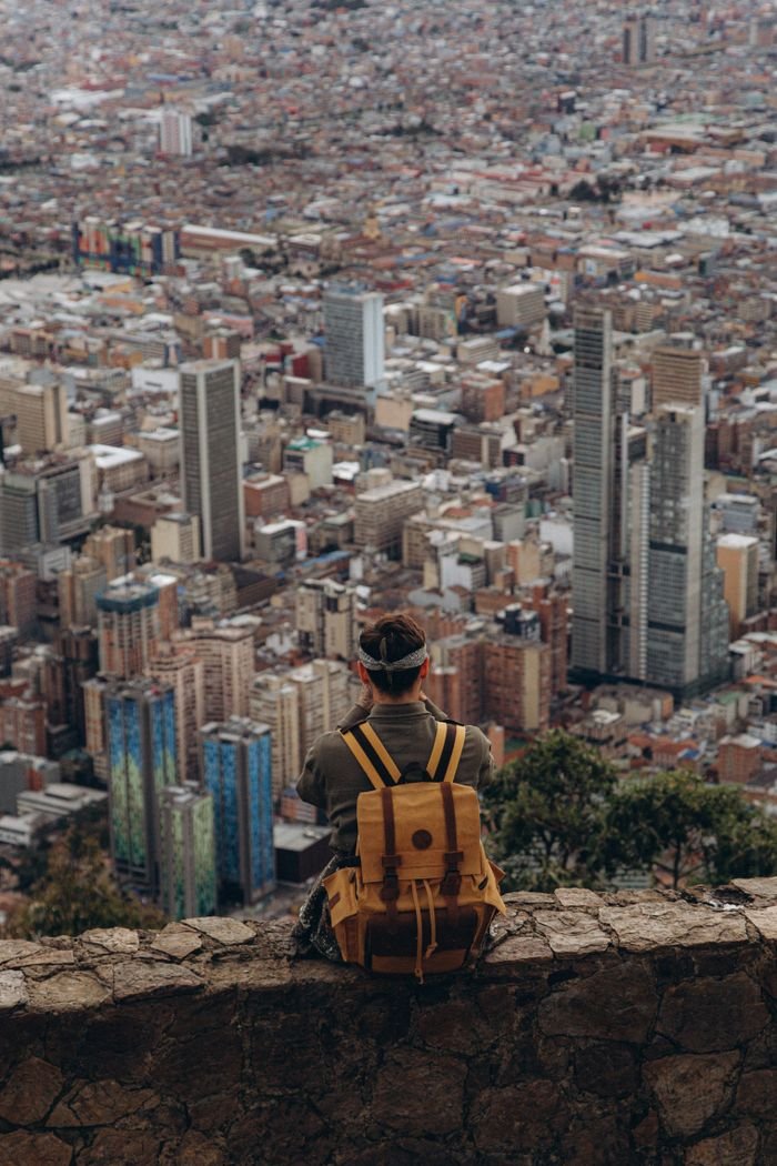 A lone traveler with a backpack sits on a ledge, viewing the city skyline.
